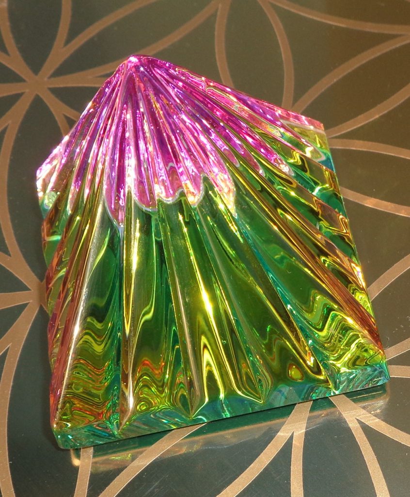 RA Lichtkristall-Pyramide: Bunte Lichtkristall-Pyramide mit facettierten Seiten auf geometrischem Hintergrund