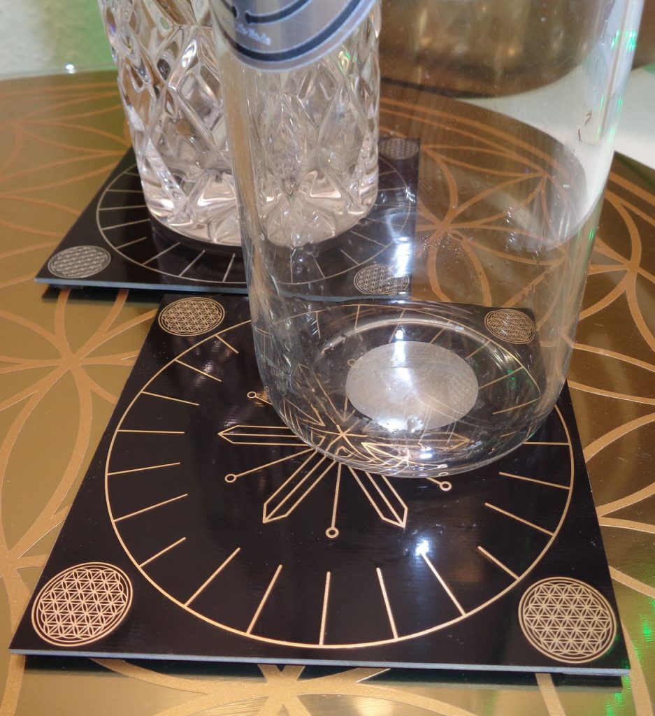 Zwei Glaskaraffen auf quadratischen schwarzen Wasser-Scheiben mit goldenen Symbolen