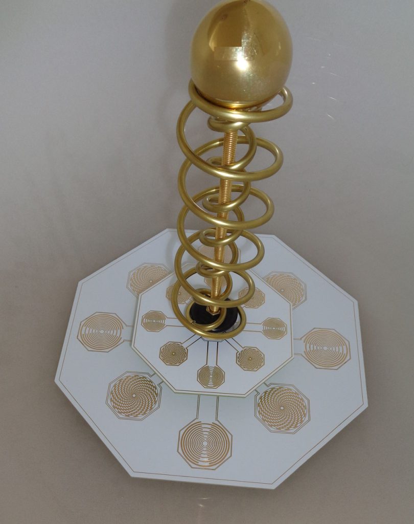 Tesla-Antenne-Mobil-DNS-SPIRIT: Goldene Tesla-Antenne auf weißer, oktogonaler Basis mit Spiralmuster