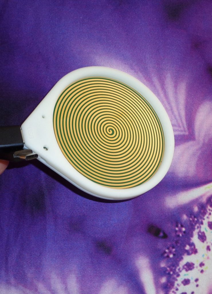 Hz-Frequenz-Disc+: Weiße Energie-Scheibe mit goldener Spirale auf violettem Hintergrund