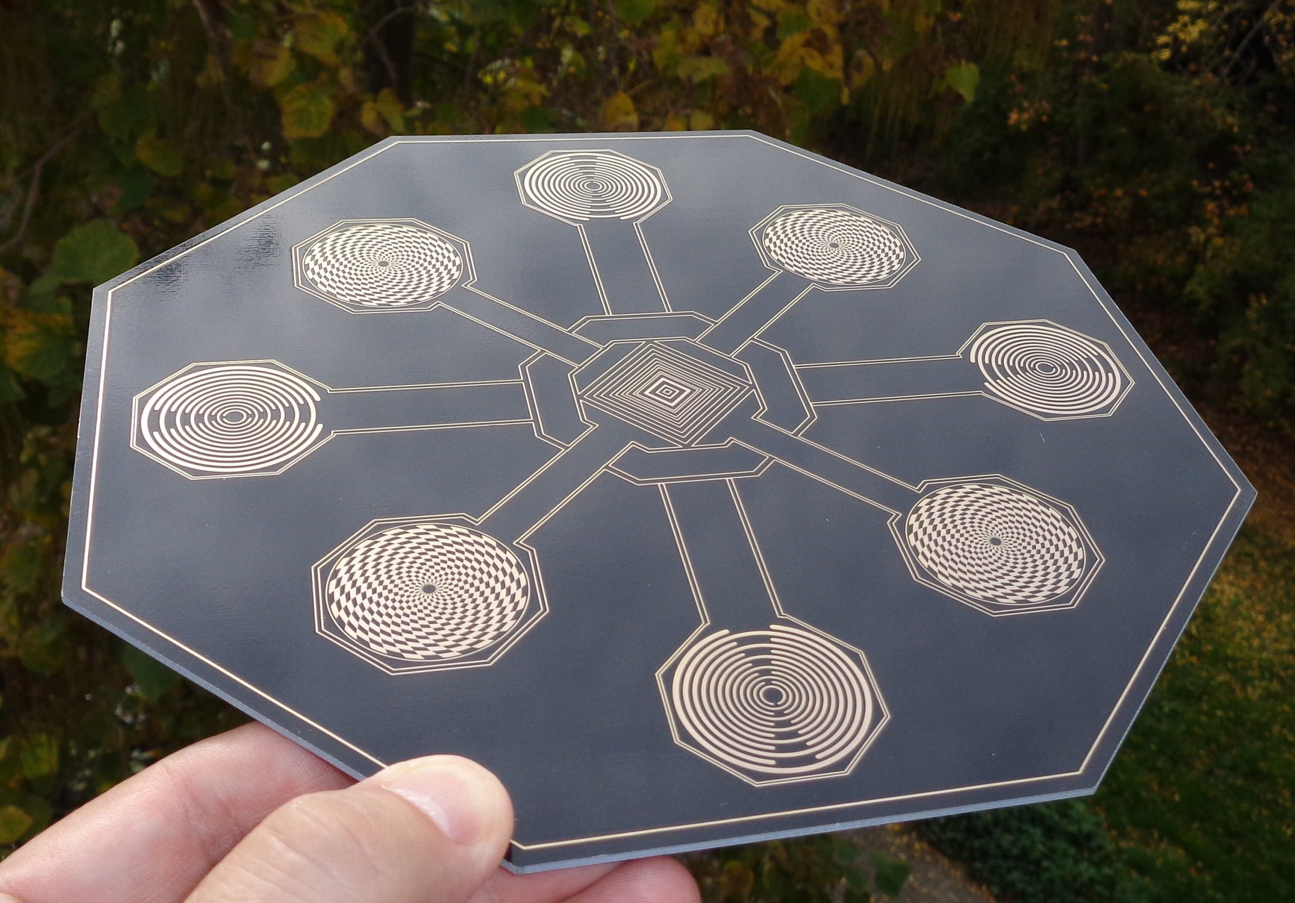 Achteckige Energie-Scheibe mit goldenen Spiralsymbolen, Hand hält sie im Freien