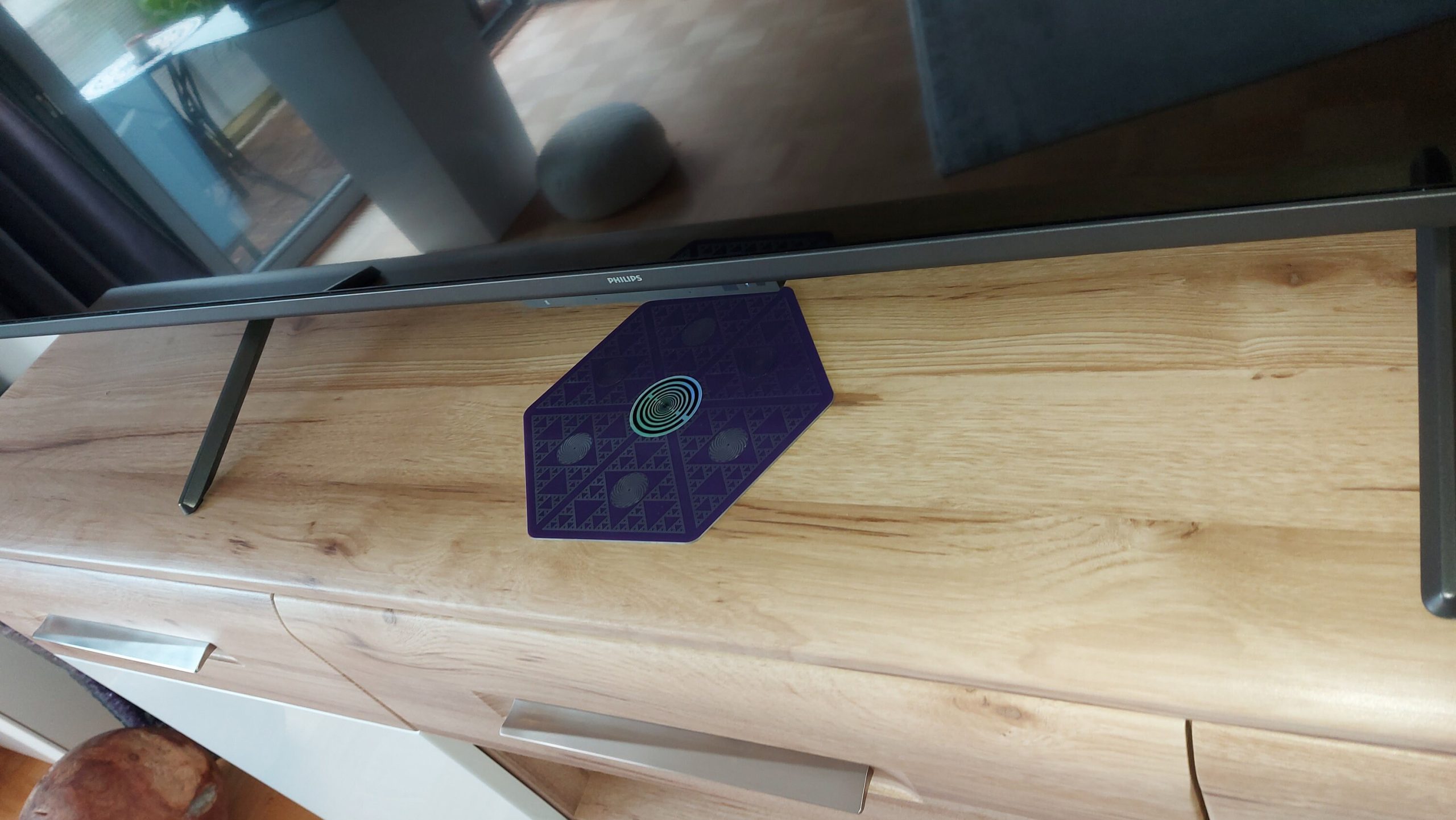 Lila Energieplatte mit geometrischen Mustern unter einem Fernseher auf Holzschrank